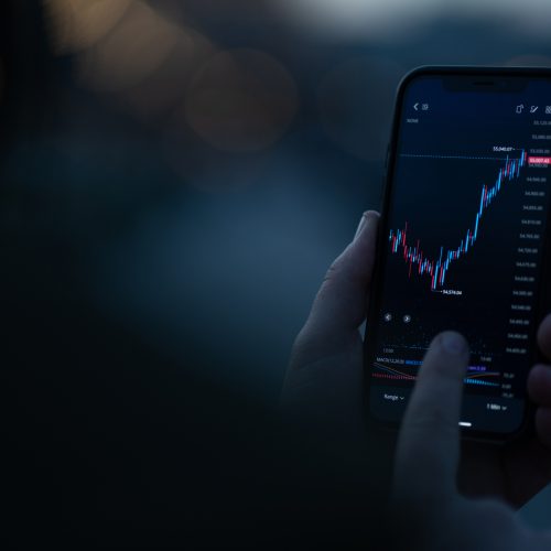 Investing online. Male hand monitoring stock exchange data on smartphone, using investment app for analyzing price activity in real time. Selective focus on mobile phone with financial chart on screen
