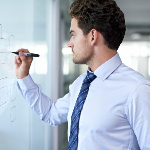Cropped view of a young businessman making a mindmap graph on a glass wall.